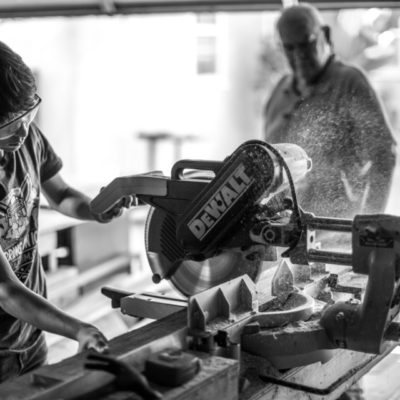 grayscale photography of boy using miter saw